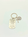 A silver-toned metal keychain featuring a dog tag engraved with a Godfather quote, a small cross, and a round St. Benedict charm, displayed on a clean off-white background.