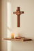 8 inch mahogany wall cross with dove hung on a cream wall above a wooden shelf with a candle and open Bible