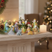 10-piece tiny pastel Nativity set displayed on a wooden mantel with warm Christmas lighting and evergreen sprigs