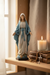 Our Lady of Grace statue displayed in a warm Catholic home prayer corner with soft natural light, a lit candle, and a rosary